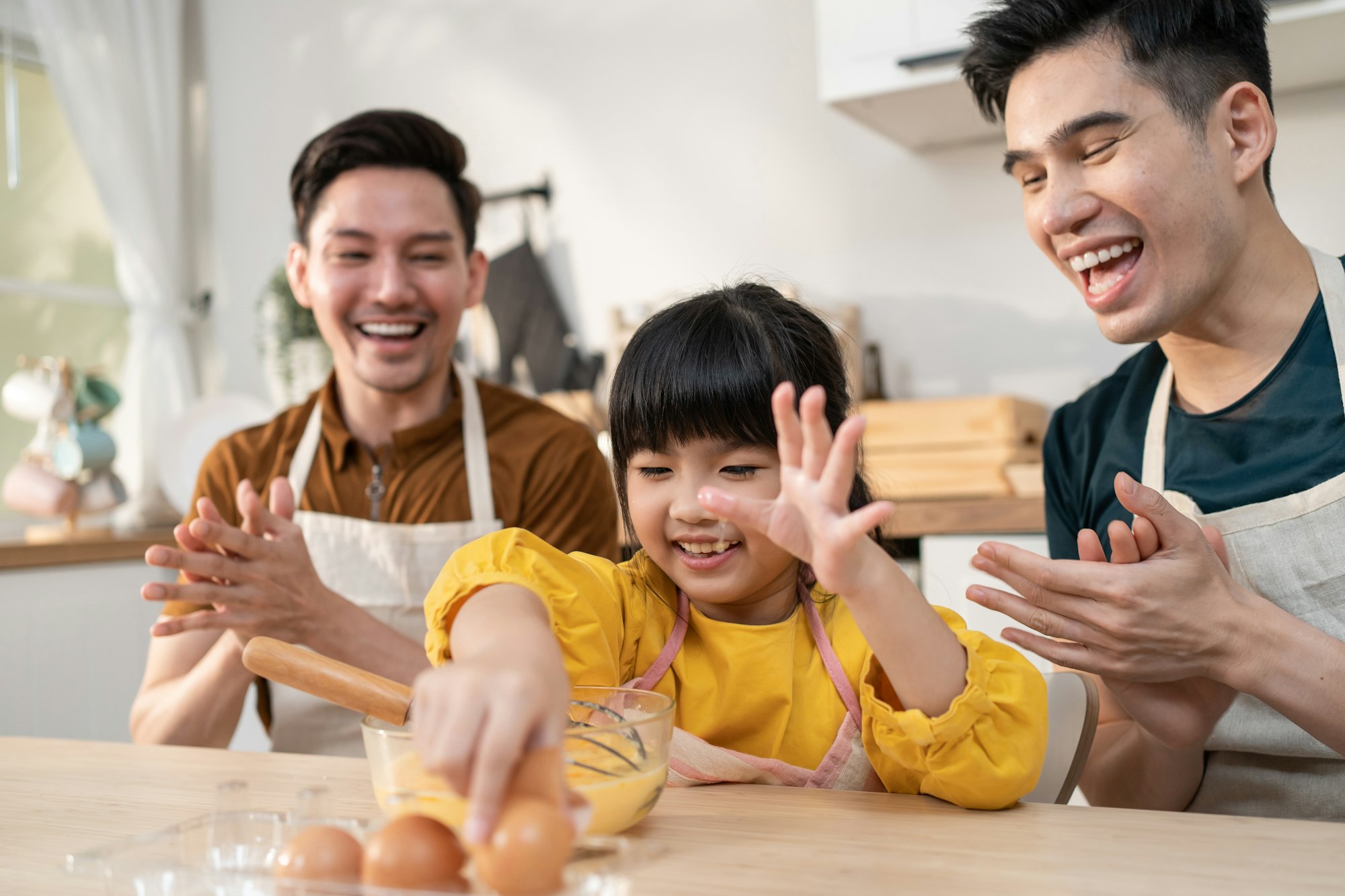 Asian LGBTQ male gay family teach girl kid stirring eggs in kitchen.